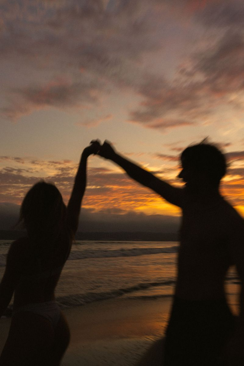 Two people dancing by the sea at sunset